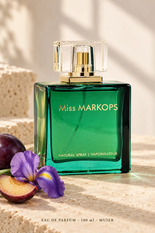 Miss Markops Eau de Parfum de 100 ml para mujer, frasco verde en perspectiva sobre fondo claro con ciruela e iris.
